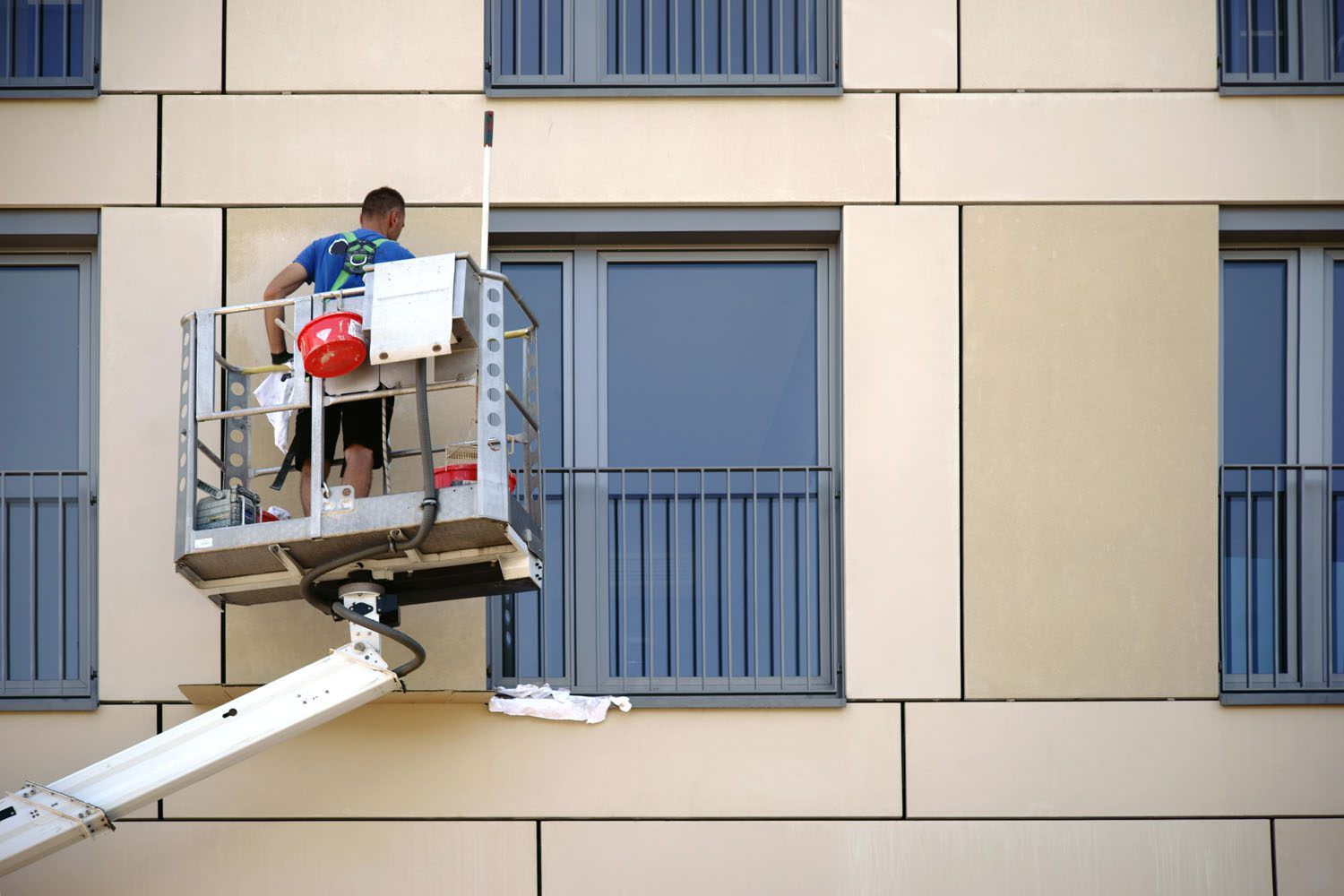 Reinigungskraft steht auf einer Hebebühne und putzt eine Häuserfassade.
