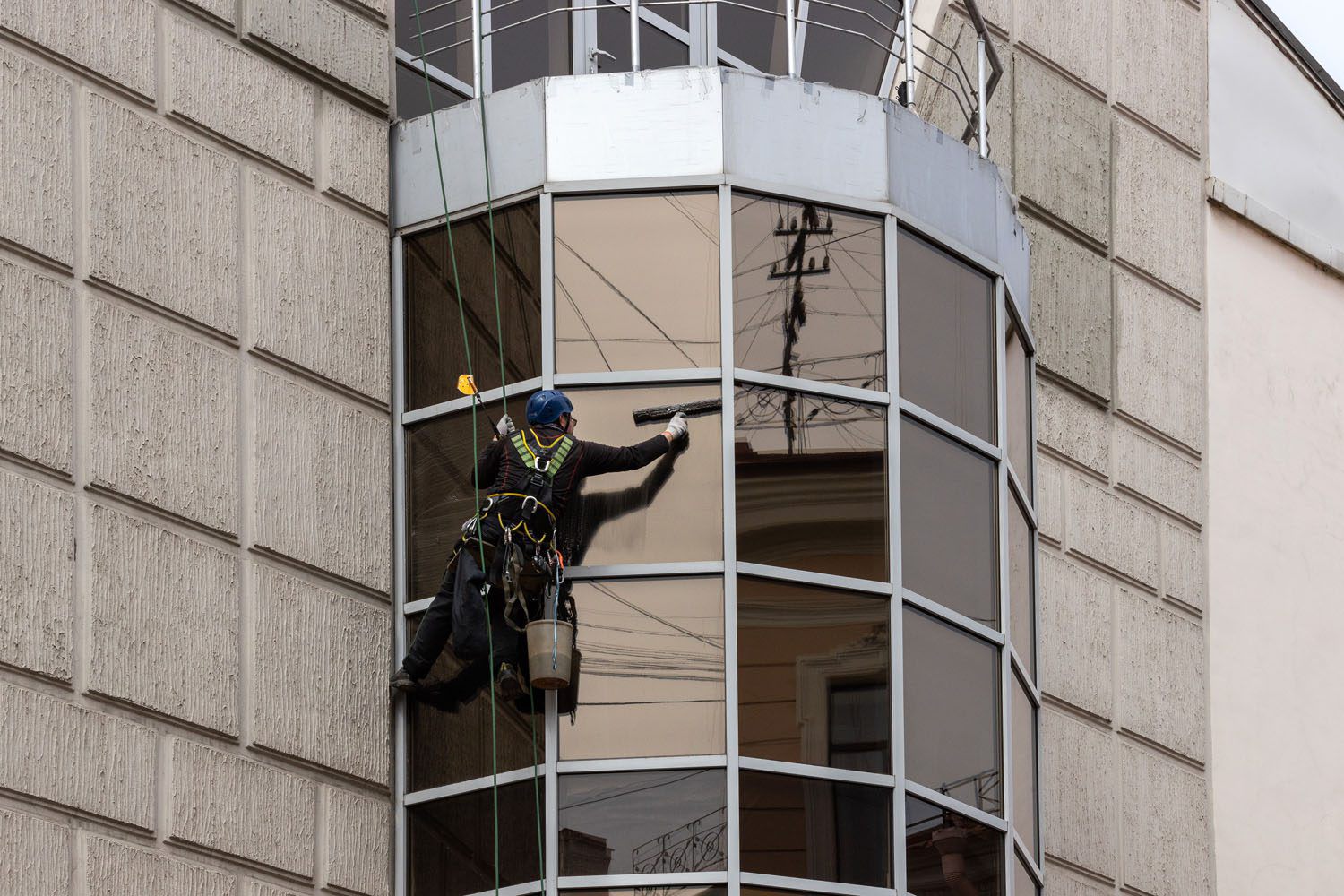 Fensterputzer hängt an einer Häuserfassade und reinigt ein Fenster.